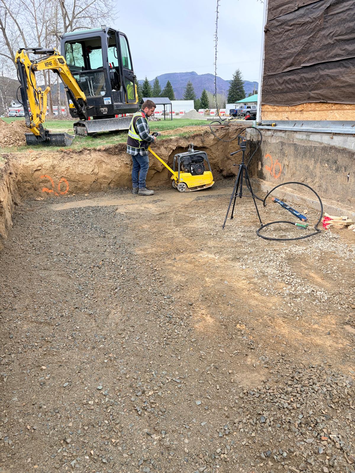 Excavator and compactor preparing ground beside an existing building